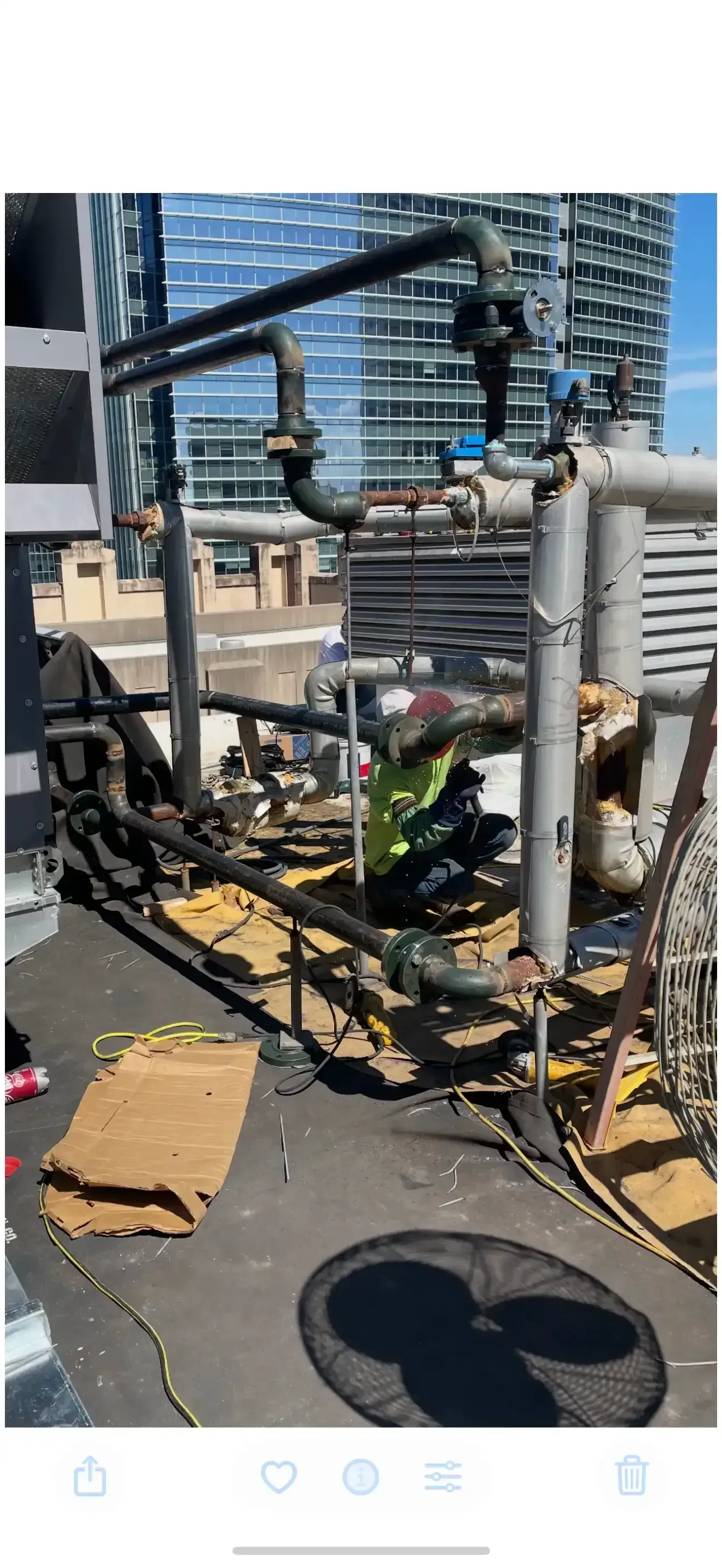 HVAC equipment on a rooftop. Black pipes, building in background. Person in green working on pipes in Las Vegas.
