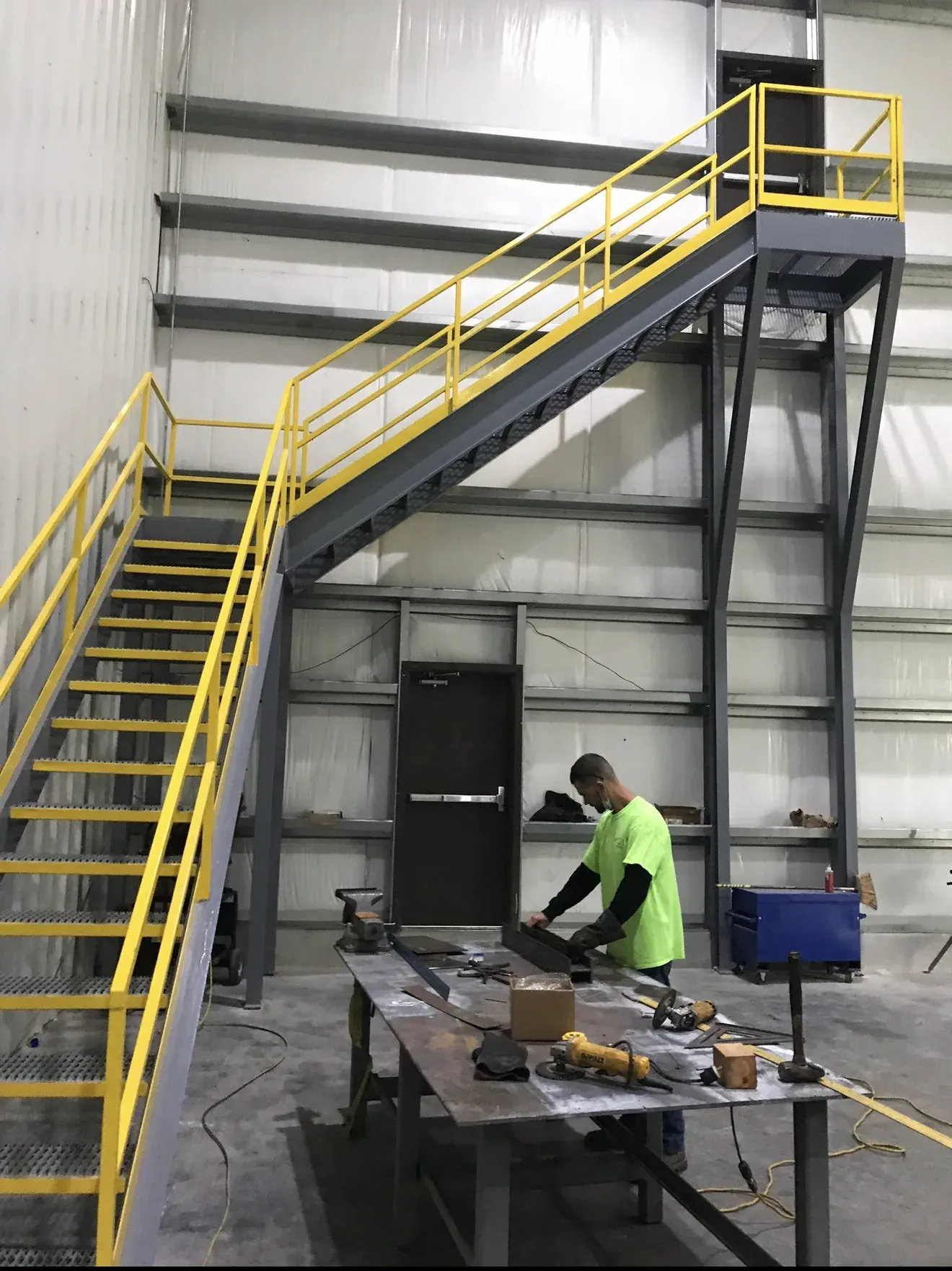 Steel staircase with yellow handrails, a worker in a neon green shirt welds metal in a factory in Las Vegas.