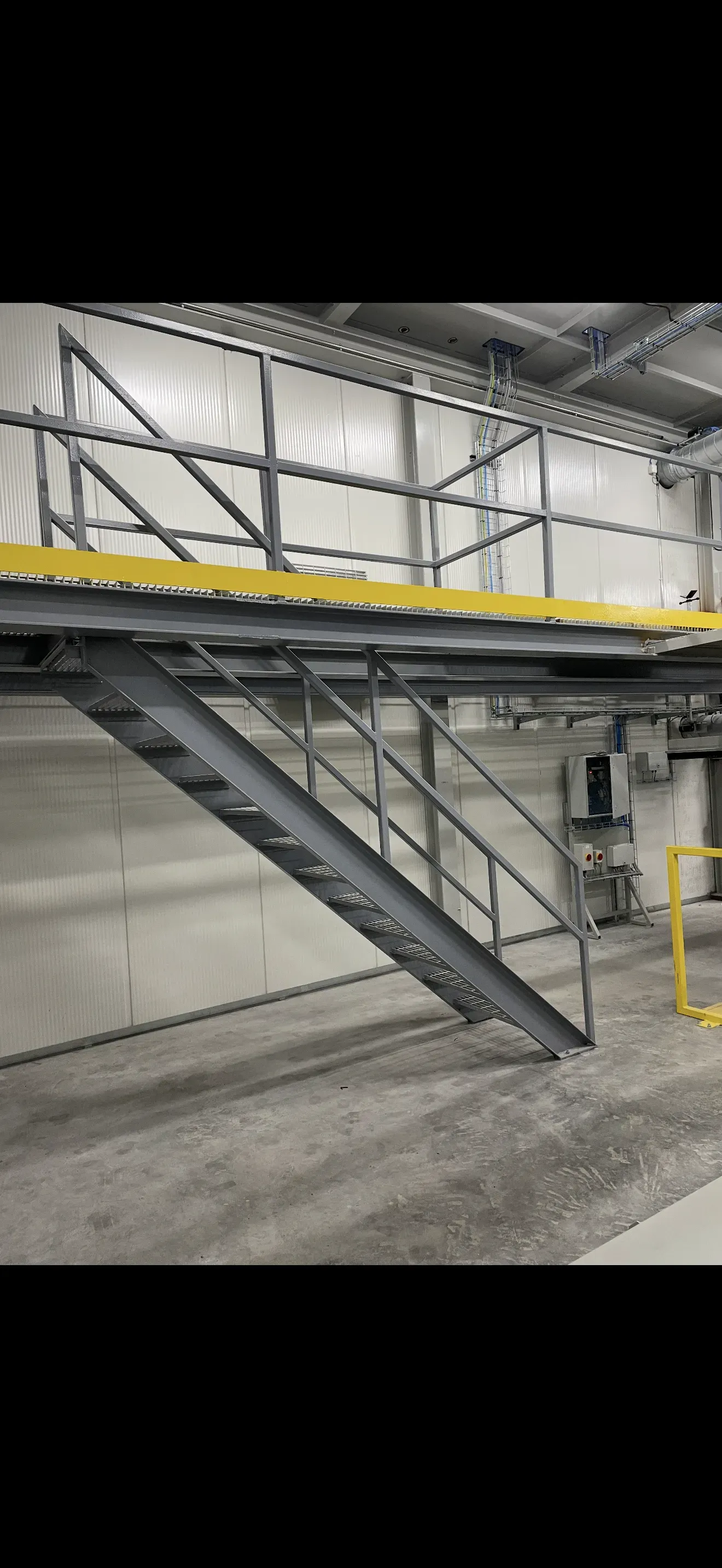Metal stairs leading to a yellow-edged platform in an industrial setting, against a concrete wall.