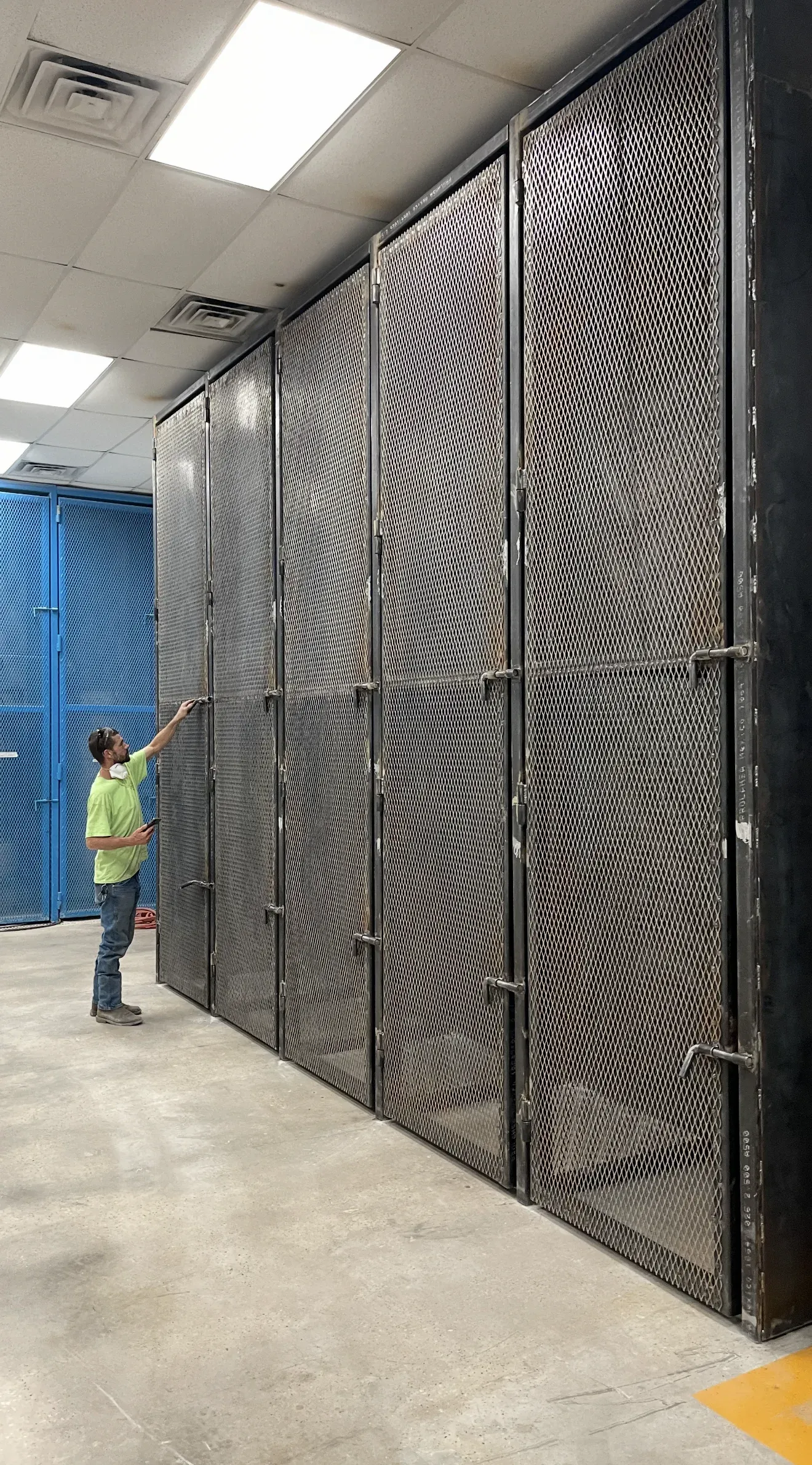 Person touching a row of tall, metal, wavy-patterned doors in a brightly lit industrial setting.