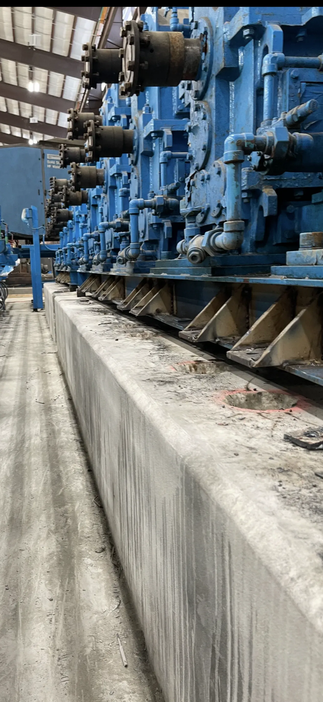 Blue industrial machinery in a factory setting. Concrete wall in foreground.